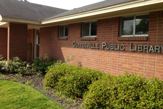 Brick Coffeeville Public Library building with shrubs along the front and the name displayed on the exterior wall.
