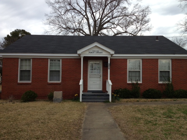 Small brick public library building with a central entrance and short walkway leading from the street.