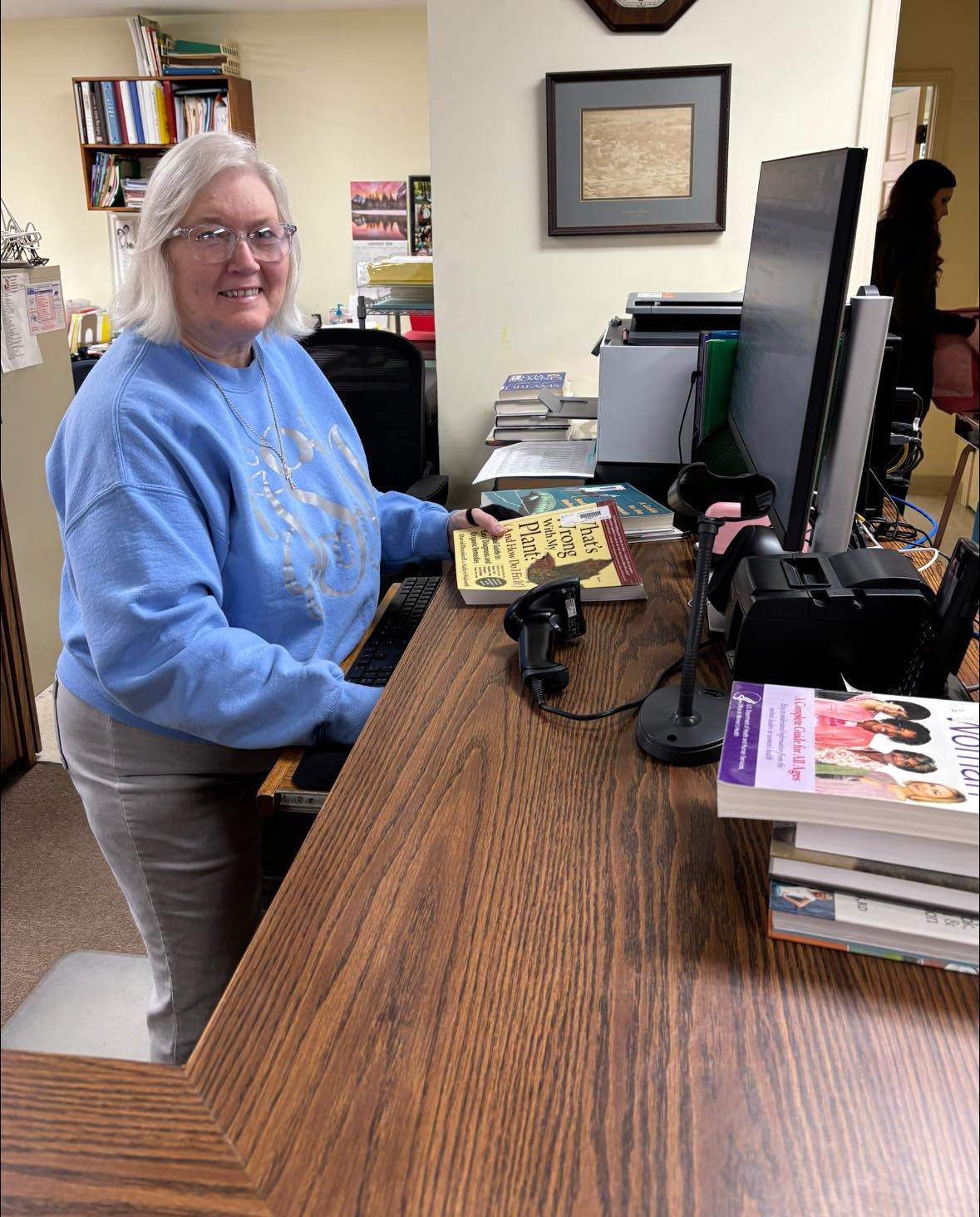Joyce standing at the library circulation desk holding a book.