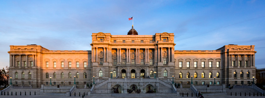 Large historic government building with grand columns and an American flag on top, illuminated at dusk.